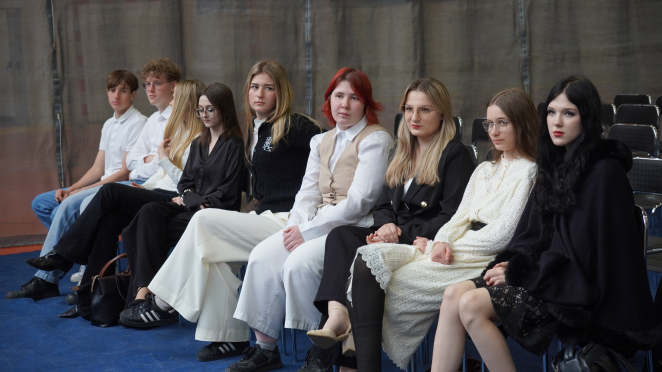 Uczniowie siedzą na krzesłach. Patrzą na wprost.