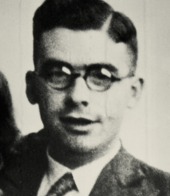 Black-and-white portrait photograph of a man, framed from the chest up. He has short hair and faces the camera. He is wearing formal clothing. The background is light.