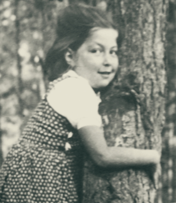 Black-and-white portrait photograph of a young girl, framed from the shoulders up. Her hair is short or tied back, and she faces the camera. The background is plain.
