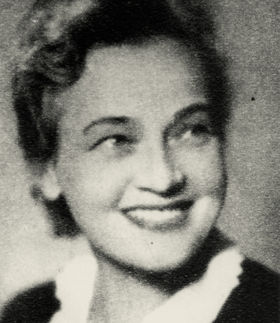 Black-and-white portrait photograph of a woman in a close-up frame. Her hair is neatly styled, and she faces the camera. She is wearing dark clothing. The background is plain.