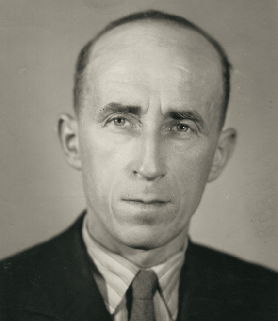 Black-and-white portrait photograph of a child or very young person in a close-up frame. The hair is short, and the face is directed toward the camera. The background is light.