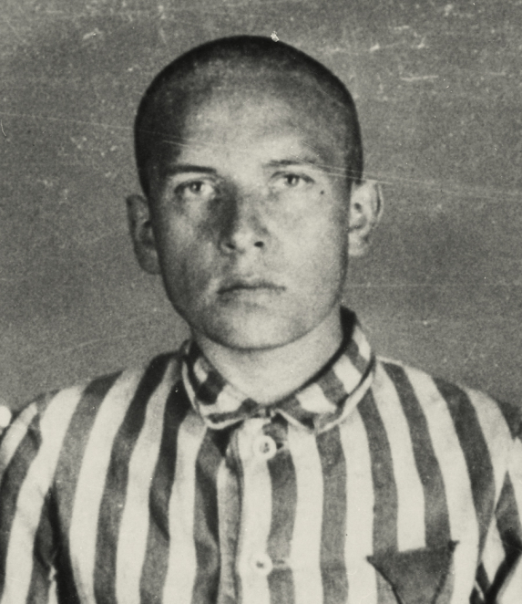 Black-and-white portrait photograph of a man, framed from the chest up. He has short hair and looks directly at the camera. He is wearing a striped prisoner unifiorm. The background is plain.
