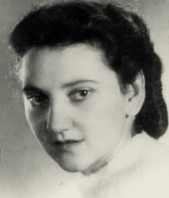 A black-and-white portrait photograph of a woman, taken from close up. Her hair is combed back or tied up, and she is facing the camera. She is wearing dark clothing. The background is light.