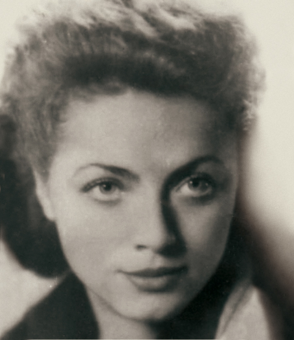A black-and-white portrait photograph of a young woman, showing her head and shoulders. She has dark hair, combed back. She is looking straight ahead. The background is plain.
