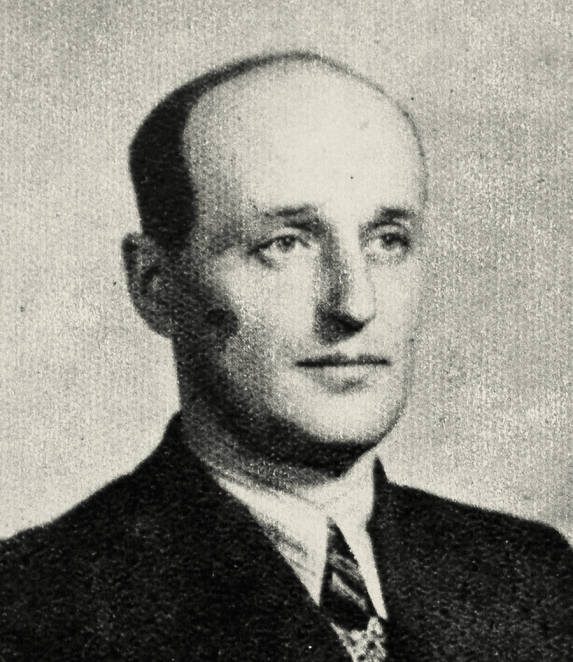 A black-and-white portrait photograph of a man, shot from the shoulders up. He has short hair and is facing the camera. He is wearing dark clothing. The background is plain.