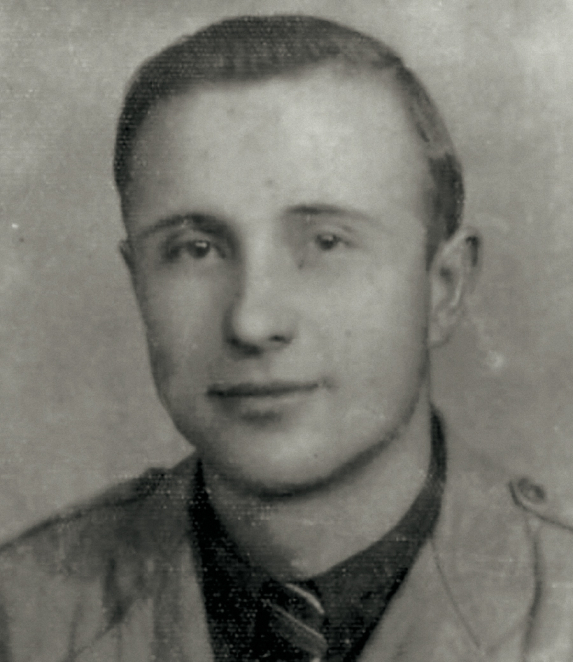 A black-and-white portrait photograph of a young man, taken in close-up. He has short hair and is looking straight ahead. He is wearing a light-coloured shirt. The background is plain.