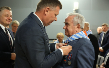 Mężczyzna w garniturze wpina medal w klapę marynarki starszego mężczyzny. 