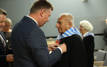 Mężczyzna w garniturze wpina medal w klapę marynarki starszego mężczyzny.