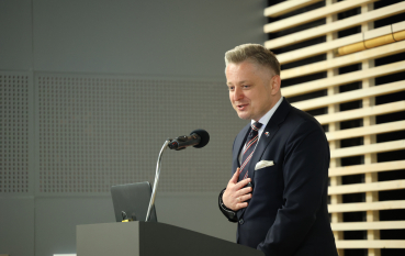 Mężczyzna w garniturze przemawia do mikrofonu. 