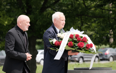 Dwóch starszych  mężczyzn składa kwiaty 