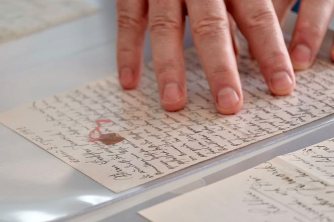 Zbliżenie na dłoń wskazującą fragment odręcznie napisanego listu z okresu II wojny światowej. Dokument jest zabezpieczony w przezroczystej koszulce archiwalnej.
